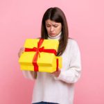 A confused woman holds a small, wrapped gift box, looking at it thoughtfully