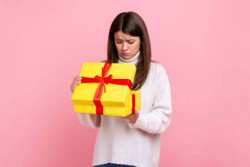 A confused woman holds a small, wrapped gift box, looking at it thoughtfully