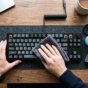 Person cleaning a mechanical keyboard with gel and a cloth on a wooden desk.
